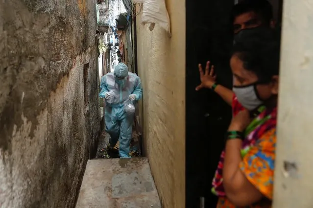 People stand at the entrance of their house as a healthcare worker wearing personal protective equipment (PPE) arrives to check the temperature of residents of a slum during a check-up camp for the coronavirus disease (COVID-19) in Mumbai, June 17, 2020. (Photo by Francis Mascarenhas/Reuters)
