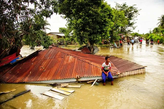 A villager sits on the roof of a flooded home in Lhokseumawe, Aceh, on October 10, 2022. (Photo by Azwar Ipank/AFP Phoot)
