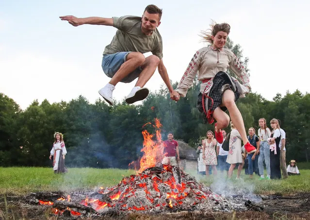 A man and a woman jump over a bonfire during Ivan Kupala Day celebrations held by the Belarusian State Museum of Folk Architecture and Rural Lifestyle in the village of Ozertso near Minsk, Belarus on July 4, 2020. Ivan Kupala Day, also known as Ivana-Kupala or Kupala Night, is a traditional pagan holiday celebrated in eastern Slavic cultures. Various rituals are traditionally performed on Kupala Night, including making flower wreaths, fortune-telling, jumping over bonfires, and burning a wheel-like effigy symbolizing the sun. (Photo by Natalia Fedosenko/TASS)