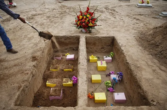 A cemetery worker shovels dirt on the remains of 14 people for whom no one came forward to claim their remains after a memorial service at St. Joseph's cemetery in  Lac Cruces, New Mexico October 7, 2015. There was little known about the people at their time of death beyond their names and dates of birth. (Photo by Shannon Stapleton/Reuters)