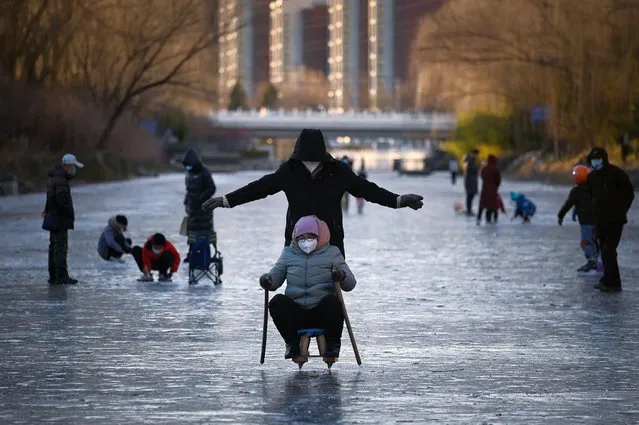 A woman and man ride on a sled on a frozen river in Beijing on December 27, 2022. (Photo by Wang Zhao/AFP Photo)