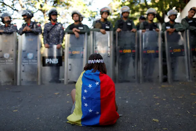A girl wears a Venezuelan flag as Venezuelan security forces block access to opposition supporters and mourners of rogue ex-policeman Oscar Perez to the main morgue of the city, in Caracas, Venezuela January 20, 2018. (Photo by Marco Bello/Reuters)