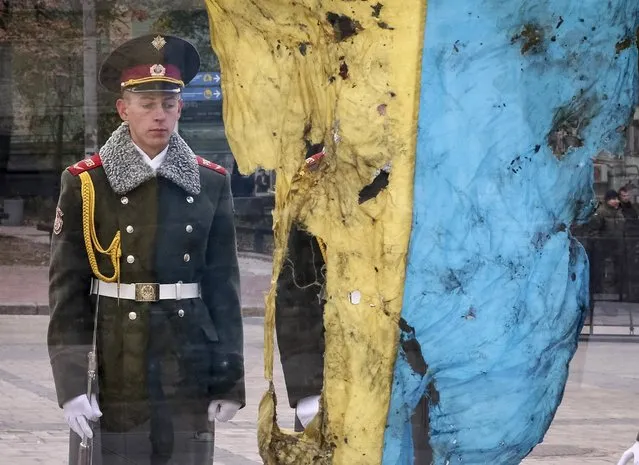 A Ukrainian soldier looks at a Ukrainian flag brought from an eastern region of the country where a military conflict took place, during the opening ceremony of an exhibition showcasing new Ukrainian military equipment in Kiev, Ukraine, October 14, 2015. The country marks Defenders Day on Wednesday. Picture taken through plastic box which the flag was displayed in. (Photo by Gleb Garanich/Reuters)