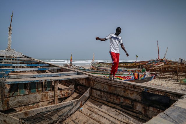 Fisherman Birane Mbaye, one of the survivors of a disastrous attempt to reach Spain last year on a boat that drifted hundreds of miles off course and ended up off the Cape Verde archipelago, walks on a large pirogue which, he says, is being restored for a possible journey to Europe, in Fass Boye, Senegal, on March 20, 2024. Adrift on the Atlantic Ocean, the migrants from West Africa resorted to drinking seawater to quench their unbearable thirst. Then they started dying one by one. Disposing of the bodies became a daily trial for those still alive on the brightly painted wooden fishing boat. “I thought I would be next, that one morning, I too would be dead and in the sea”, said Mbaye, one of 101 men and boys who set off from a fishing village on a wild stretch of Senegal's coastline last July hoping to reach Europe. They never made it. (Photo by Zohra Bensemra/Reuters)