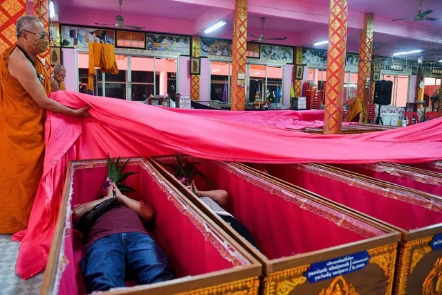 Devotees lie down and pray inside coffins to get rid of bad luck and to reborn again for a fresh start in the New Year at a temple in Nonthaburi, in the outskirt of Bangkok, Thailand on January 2, 2023. (Photo by Chalinee Thirasupa/Reuters)