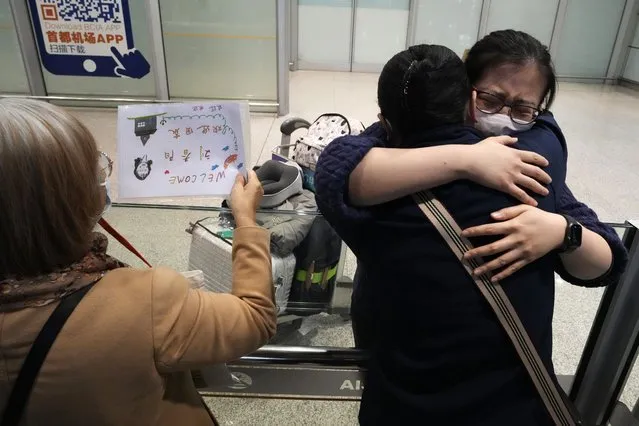 A woman hugs another returning on one of the few overseas flight arriving at the Beijing Capital International Airport in Beijing, Tuesday, March 14, 2023. China will reopen its borders to tourists and resume issuing all visas Wednesday after a three-year halt during the pandemic as it sought to boost its tourism and economy. (Photo by Ng Han Guan/AP Photo)