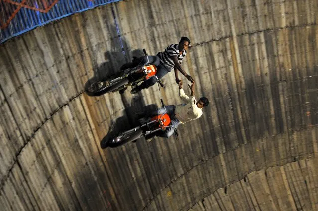 Stunt performers ride their motorcycles on the walls of the "Well of Death", at a fair on the outskirts of Bengaluru, India, November 5, 2015. The performers earn their livelihood by performing daredevil stunts such as driving their bikes and cars on the walls of the "Well of Death" attraction, which draws a large number of spectators. (Photo by Abhishek N. Chinnappa/Reuters)
