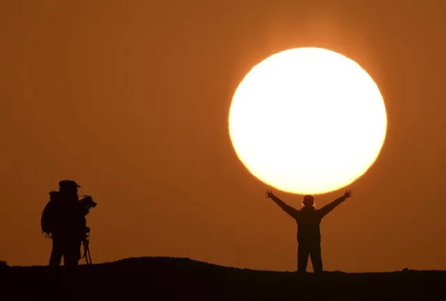 A tourist poses for photographs in front of the rising sun at a tourist resort in Bayingolin Mongol Autonomous Prefecture, Xinjiang Uighur Autonomous Region, China, October 3, 2015. (Photo by Reuters/China Daily)