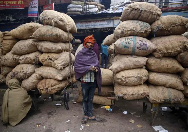 A worker prepares his chewing tobacco while standing in front of sacks at a wholesale grocery market on a winter morning in the old quarters of Delhi December 19, 2014. (Photo by Ahmad Masood/Reuters)