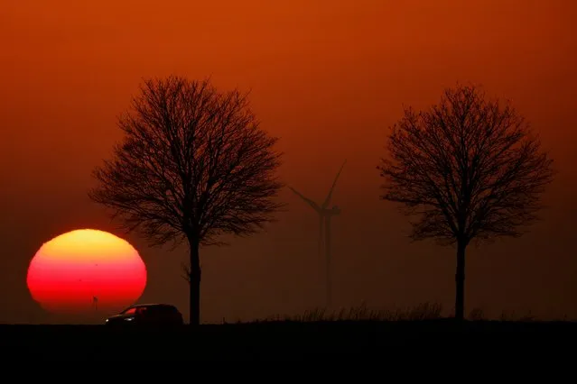 A car drives in front of power-generating windmill turbines on the Cambrai-Arras road during sunset in Epinoy, France on February 15, 2023. (Photo by Pascal Rossignol/Reuters)