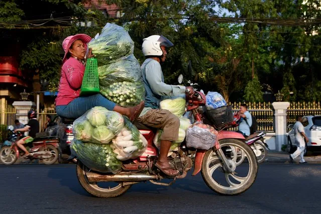 A woman holds piles of vegetables transported by motorcycle along a street in Phnom Penh, Cambodia on January 22, 2020. (Photo by Tang Chhin Sothy/AFP Photo)