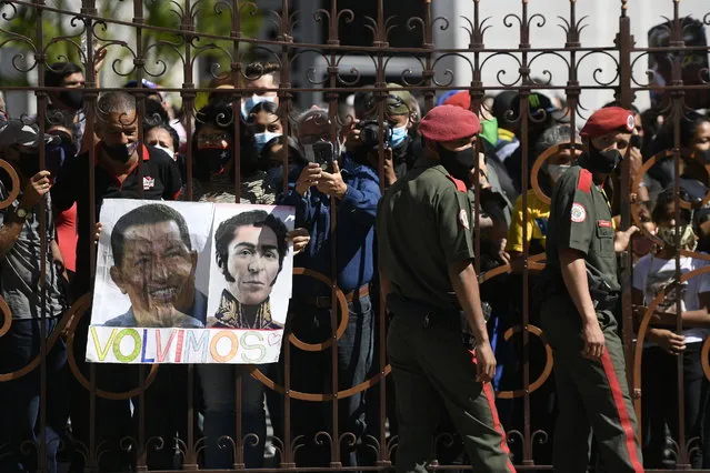 Government supporters, one with photos of late Venezuelan President Hugo Chavez, left, and independence hero Simon Bolivar with the Spanish message “We're back”, stand outside the National Assembly where lawmakers are being sworn-in, in Caracas, Venezuela, Tuesday, January 5, 2021. (Photo by Matias Delacroix/AP Photo)