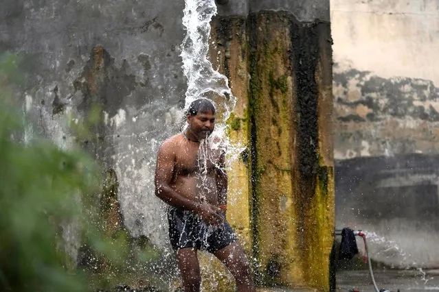 A man bathes from a roadside water tap to cool himself on a hot summer day on the outskirts of Jammu, India, Tuesday, May 16, 2023. (Photo by Channi Anand/AP Photo)