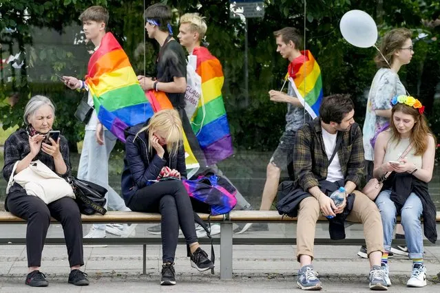 People sit on a bench as participants in Poland's yearly Pride parade, known as the Equality Parade, walk by in Warsaw, Poland, on Saturday June 17, 2023. This year's event was dedicated to transgender rights, which are facing a backlash in many countries. (Photo by Czarek Sokolowski/AP Photo)