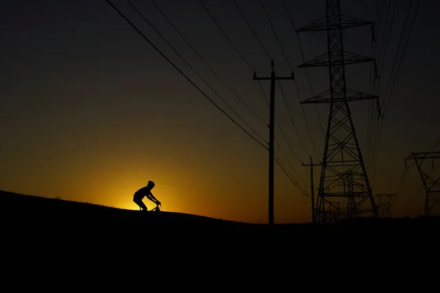 A cyclist passes under power lines during an evening ride, Monday, June 26, 2023, in San Antonio. Meteorologists say scorching temperatures brought on by a heat dome have taxed the Texas power grid and threaten to bring record highs to the state. (Photo by Eric Gay/AP Photo)