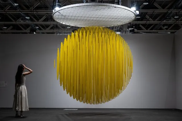 A visitor watches “Esfera Amarilla” 1984, painted metal and nylon thread by late Venezuelan artist Jesus Rafael Soto displayed at the Art Basel fair for Modern and contemporary art, in Basel, Switzerland on June 13, 2023. The fair will take place from June 15 to June 18, 2023. (Photo by Fabrice Coffrini/AFP Photo)