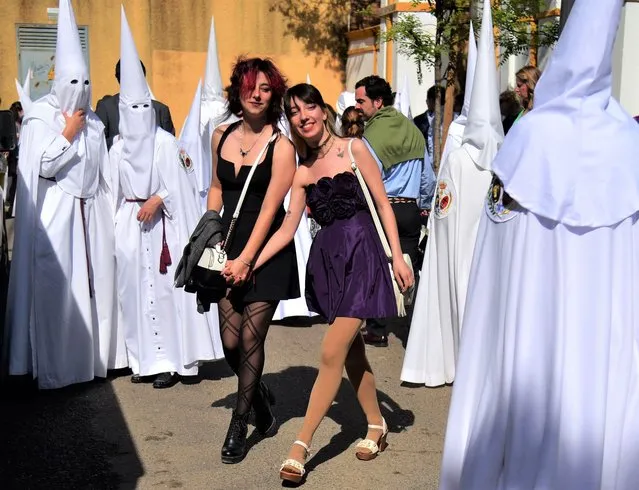Two women walk among penitents of “La Paz” brotherhood as they gather for the Palm Sunday procession during the Holy Week in Seville on April 10, 2022. Christian believers around the world mark the Holy Week of Easter in celebration of the crucifixion and resurrection of Jesus Christ. (Photo by Cristina Quicler/AFP Photo)