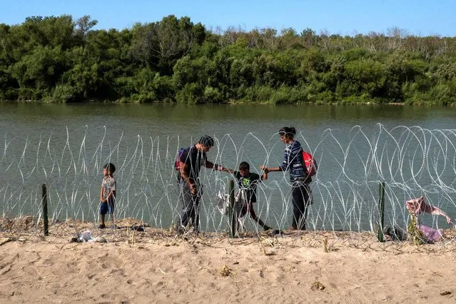 A family navigates the bank of the Rio Grande past razor wire while searching for an entry point into the United States from Mexico, in Eagle Pass, Texas, U.S. July 30, 2023. (Photo by Adrees Latif/Reuters)