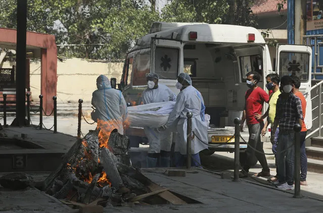 Health workers carry a body of a person who died of COVID-19 for cremation, in New Delhi, India, Monday, April 19, 2021. New Delhi imposed a weeklong lockdown Monday night to prevent the collapse of the Indian capital's health system, which authorities said had been pushed to its limit amid an explosive surge in coronavirus cases. (Photo by Manish Swarup/AP Photo)