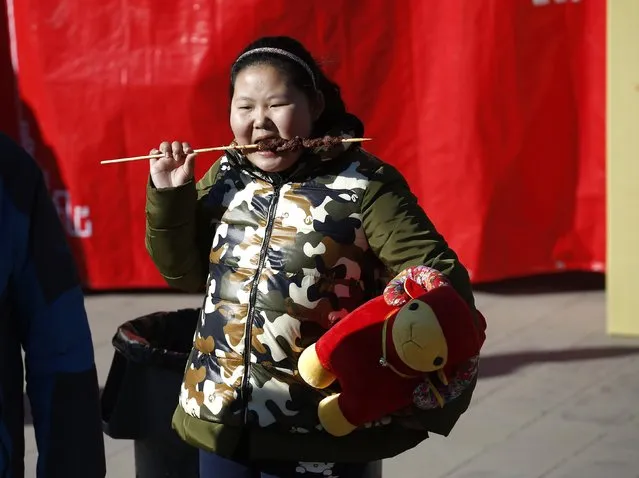 A girl, holding a sheep toy, eats at the Temple Fair, which is part of Chinese New Year celebrations at Ditan Park, also known as the Temple of Earth, in Beijing, February 18, 2015. (Photo by Kim Kyung-Hoon/Reuters)