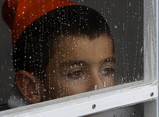A refugee boy looks out of a window of a tent covered in raindrops, at the transit center for refugees near the northern Macedonian village of Tabanovce, while he waits with his family for permission to cross the border into Serbia, February 24, 2016. Hundreds of migrants from Afghanistan and other nations remain stranded on borders of Macedonia with Serbia, unable to cross, and some of them forced backward toward Greece. (Photo by Boris Grdanoski/AP Photo)