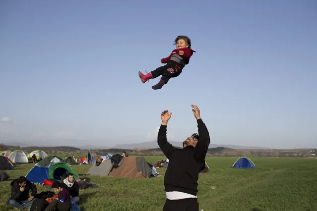 A Syrian man plays with his one-year child as refugees and migrants wait to be allowed to cross the border to Macedonia in the northern Greek border station of Idomeni on, Tuesday, March, 1 2016. Some 7,000 migrants, including many from Syria and Iraq, are crammed into a tiny camp at the Greek border village of Idomeni, and hundreds more are arriving daily. (Photo by Petros Giannakouris/AP Photo)