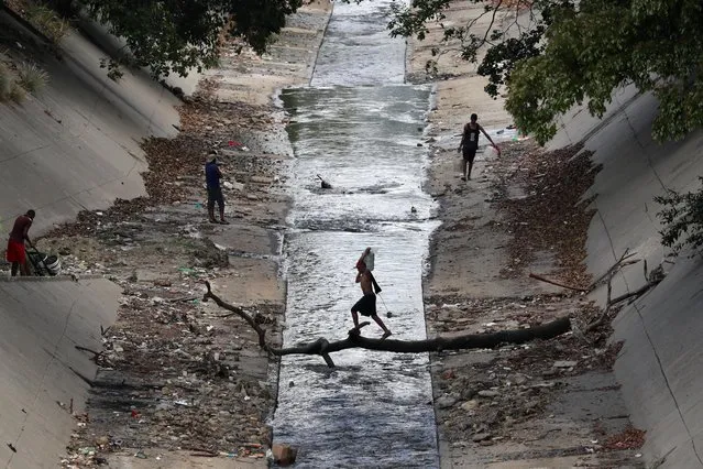 A local carries a water container as he crosses a river in Caracas, March 12, 2019. (Photo by Ivan Alvarado/Reuters)