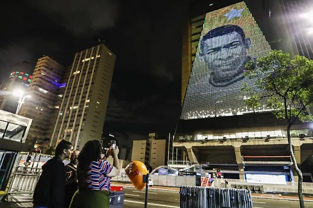 A woman takes a photo of the image of late soccer player Pele, reproduced on the building of the Federation of Industries of Sao Paulo, in Sao Paulo, Brazil, Thursday, December 29, 2022. Pele, who played most of his career with Santos FC, has died in Sao Paulo. (Photo by Marcelo Chello/AP Photo)