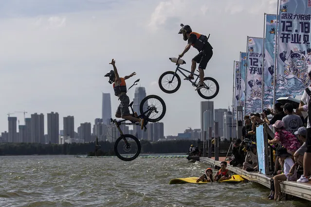 The two extreme cycling enthusiast performs a stunt with a bicycle before falling into the East Lake on September 25, 2021 in Wuhan, Hubei province, China. This activity, which requires participants to ride their bikes and jump into the lake, attracts many extreme cycling enthusiasts from the city. The event is in its 11th year. (Photo by Getty Images)