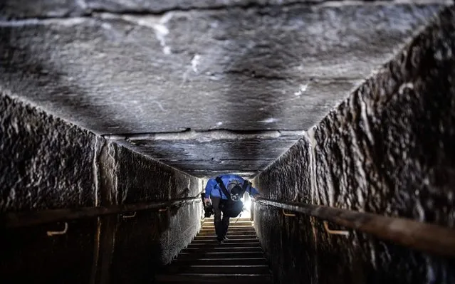 A man walks through a passage in the well-known bent pyramid of King Snefru, which had been closed to visitors since 1965, in Dahshur, some 30 kilometres (20 miles) south of Cairo, on July 13, 2019, after it was reopened by the Egyptian Antiquities Minister. Egyptian archaeologists unveiled Saturday several sarcophagi with some containing well-preserved mummies, along with the remains of an ancient wall dating to the Middle Kingdom nearly 4,000 years ago. The finds were made during excavation work in the ancient royal necropolis of Dahshur on the west bank of the Nile River, south of Cairo. The area is home to some of Egypt's oldest pyramids including the bent pyramid of King Sneferu, the first pharaoh of Egypt's 4th dynasty. (Photo by Mohamed el-Shahed/AFP Photo)