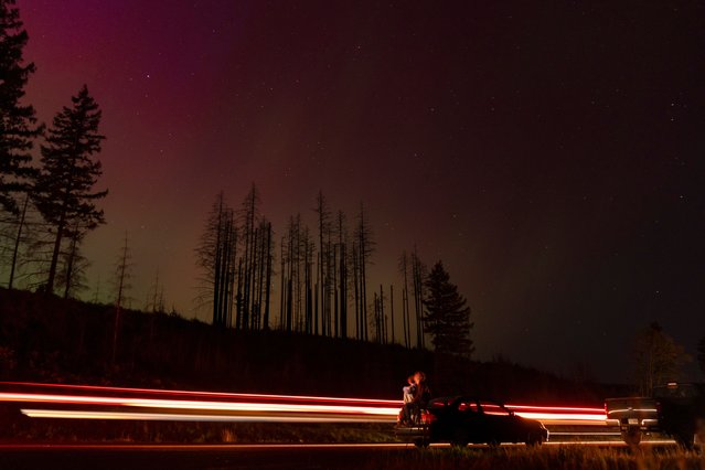 In this image taken with a long exposure, cars pass by as people look at the night sky towards the northern lights, or Aurora Borealis, on Friday, May 10, 2024, in Estacada, Ore. Brilliant purple, green, yellow and pink hues of the Northern Lights were reported worldwide, with sightings in Germany, Switzerland, London, and the United States and Canada. (Photo by Jenny Kane/AP Photo)
