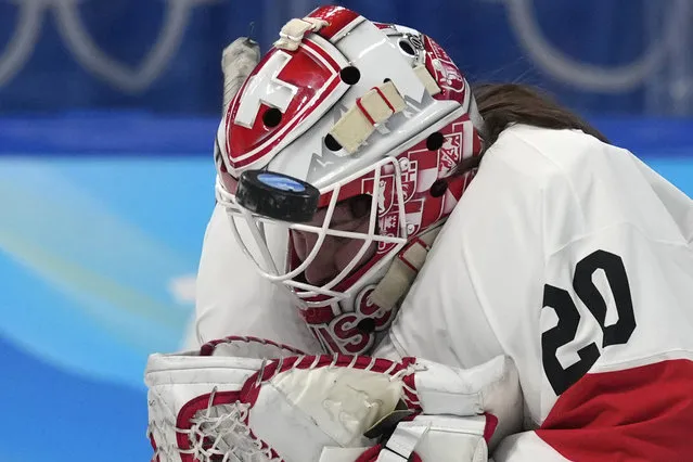 The puck hits the mask of Switzerland goalkeeper Andrea Braendli during the women's bronze medal hockey game against Finland at the 2022 Winter Olympics, Wednesday, February 16, 2022, in Beijing. (Photo by Petr David Josek/AP Photo)