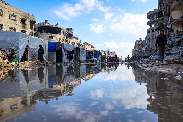 Displaced Palestinians walk around a puddle in front of destroyed buildings and tents in Khan Yunis in the southern Gaza Strip on May 16, 2024, amid the ongoing conflict between Israel and the militant group Hamas. (Photo by AFP Photo/Stringer)