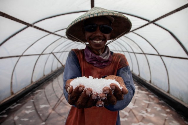 A worker poses with salt as they harvest salt from seawater in a greenhouse, which allows year-round salt production and produces higher quality without dust and rainwater inclusions, in Bungko, West Java, on June 1, 2024. (Photo by Aditya Irawan/AFP Photo)