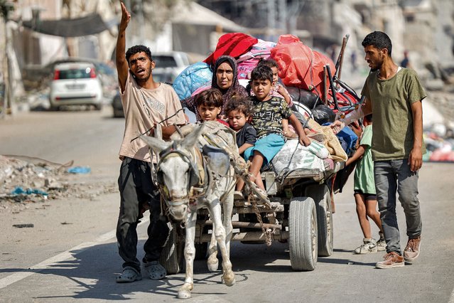 A man gestures while leading a donkey pulling a cart transporting his family members and belongings as they try to return to their home in the Tuffah district east of Gaza City on July 8, 2024 amid the ongoing conflict in the Palestinian territory between Israel and Hamas. (Photo by Omar Al-Qattaa/AFP Photo)