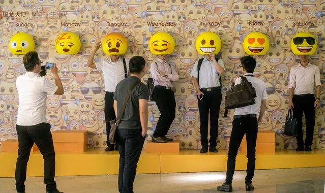 People pose for photos with emoji masks fixed onto a wall at a shopping mall in Guangzhou in south China's Guangdong province, Thursday, May 26, 2016. Emoji icons are popularly used for social media communication as they transcend cultural barriers and are fun to use. (Photo by Chinatopix via AP Photo)