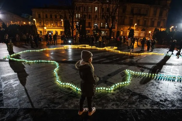 A girl stands in front of lit candles forming the shape of Ukraine's map, in memory of lost lives, in front of the Taras Shevchenko monument, in Lviv, western Ukraine, late Tuesday, April 5, 2022. (Photo by Nariman El-Mofty/AP Photo)