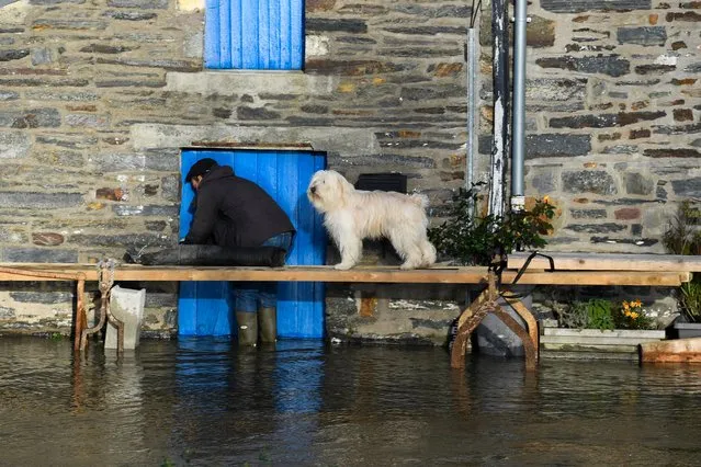 A man checks the door of a house next to a dog staning on a footbridge over the flooded streets on the centre of Guipry-Messac, western France on December 23, 2019, after La Vilaine river bursts its banks due to heavy rains. (Photo by Damien Meyer/AFP Photo)
