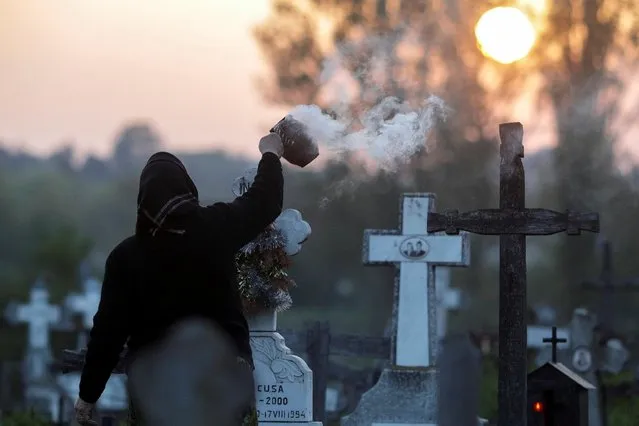 A woman burns incense near the grave of departed relatives in a cemetery south west of Romanian capital Bucharest, in the early hours of Maundy Thursday, in Copaciu, Romania, April 25, 2019. (Photo by Octav Ganea/Inquam Photos via Reuters)