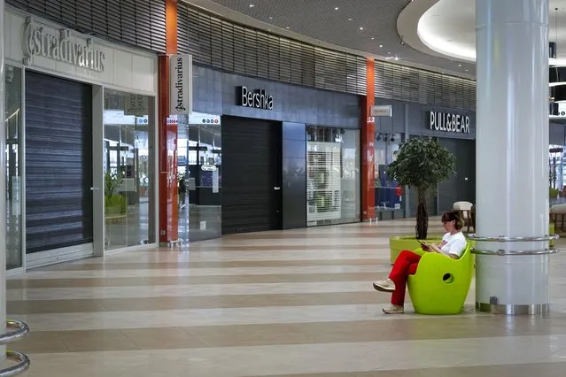 A woman sits looking at her smartphone in front of shops closed due to sanctions in a mall in St. Petersburg, Russia, Tuesday, June 1, 2022. Many Western retailers have left Russia after the start of a military action in Ukraine. (Photo by Dmitri Lovetsky/AP Photo)