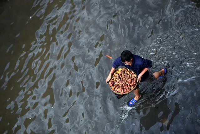 A man carries a basket with wild mushrooms as he walks on a flooded street after a rainstorm in Kunming, China July 15, 2017. (Photo by Li Jinhong/Reuters/CNS)