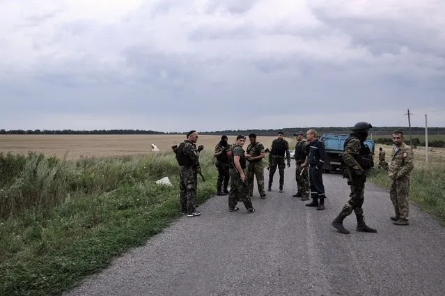 People wearing military fatigues, stand on a road,  on July 17, 2014 at the site of the crash of a malaysian airliner carrying 295 people from Amsterdam to Kuala Lumpur, near the town of Shaktarsk, in rebel-held east Ukraine. (Photo by Dominique Faget/AFP Photo)