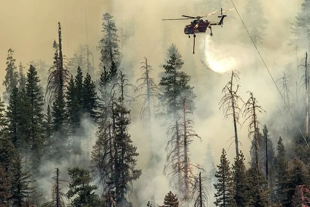 Seen from unincorporated Mariposa County, Calif., a helicopter drops water on the Washburn Fire burning in Yosemite National Park, Saturday, July 9, 2022. (Photo by Noah Berger/AP Photo)