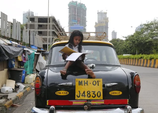 A girl studies while sitting on top of a taxi outside her shanty home at a roadside in Mumbai, India, August 11, 2015. (Photo by Shailesh Andrade/Reuters)