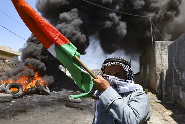 An elderly Palestinian man holds a national flag during clashes with Israeli forces following a demonstration against the expropriation of Palestinian land by Israel, in the village of Kfar Qaddum near the Jewish settlement of Kedumim in the occupied West Bank, on July 1, 2022. (Photo by Jaafar Ashtiyeh/AFP Photo)