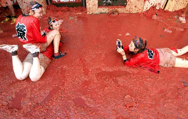 Two woman have their photo taken as they pose in a puddle of squashed tomatoes during the annual “Tomatina” tomato fight fiesta, in the village of Bunol, 50 kilometers outside Valencia, Spain, Wednesday, August 26, 2015. The streets of an eastern Spanish town are awash with red pulp as thousands of people pelt each other with tomatoes in the annual “Tomatina” battle that has become a major tourist attraction. (Photo by Alberto Saiz/AP Phot)