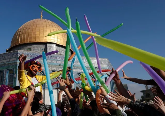 A man dressed in a clown outfit distributes balloons to children by the Dome of the Rock inside al- Aqsa Mosque compound, in Jerusalem' s old city on the first day of Eid al- Adha on September 1, 2017. (Photo by Ahmad Gharabli/AFP Photo)
