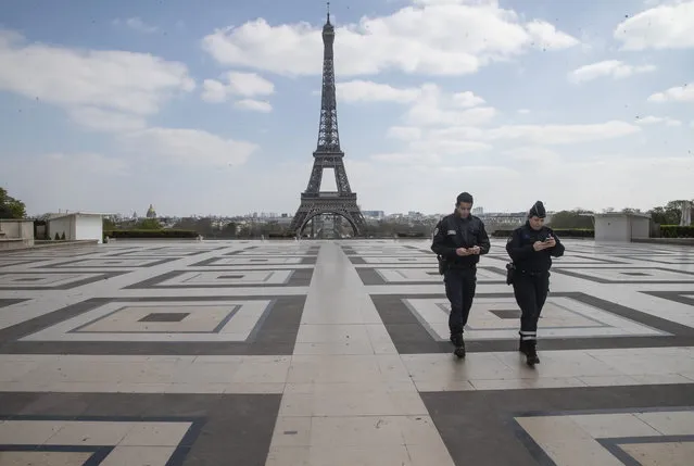 Police officers checks their phones as they walk on Trocadero plaza during a nationwide confinement to counter the new coronavirus, in Paris, Thursday, April 2, 2020. (Photo by Michel Euler/AP Photo)