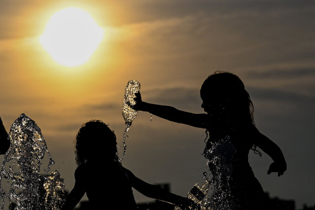 Children cool off by playing in a fountain in Domino Park, Brooklyn with the Manhattan skyline in the background as the sun sets during a heat wave on July 24, 2022 in the Brooklyn borough of New York City. The five boroughs of New York City are under a heat advisory until 8 PM on July 24th according to the US National Weather Service. Much of the East Coast is experiencing higher than usual temperatures as a heat wave moves through the area forcing residents into parks, pools and beaches to escape the heat. (Photo by Alexi Rosenfeld/Getty Images)