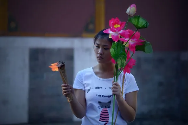 A woman holds a bunch of burning incense sticks and artificial flower during the Mid-Autumn festival at Lama Temple in Beijing on September 8, 2014.  As a tranditonal custom, thousands of Chinese people head to temples to offer prayers during the festival in Beijing. (Photo by Wang Zhao/AFP Photo)